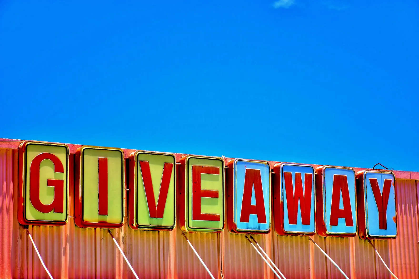 Vintage illuminated GIVEAWAY sign mounted on a wall against a clear blue sky