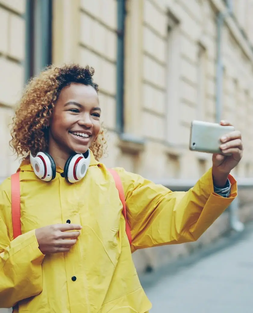 Smiling woman in a yellow raincoat recording a selfie video on her phone