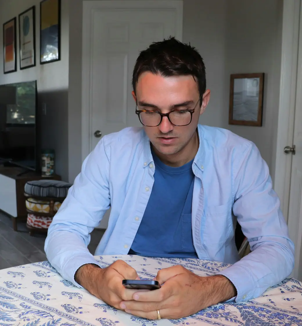 Man in glasses reading replies on his phone at a table