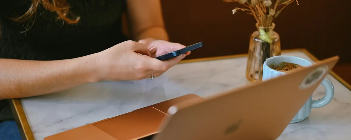 Person replying on a smartphone at a marble table beside a laptop and flowers