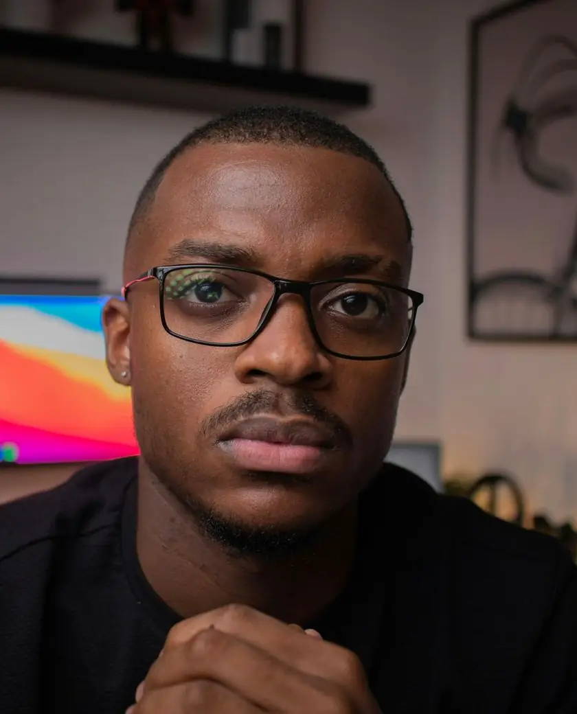 YouTube creator in glasses at his desk with a colorful monitor glowing behind him