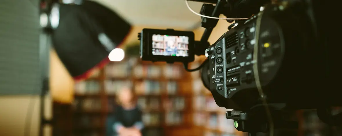 Video camera with a monitor filming a YouTube creator in a studio lined with bookshelves